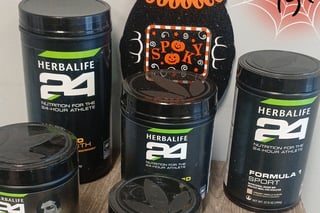 Collection of Herbalife 24 sports nutrition products displayed with Halloween-themed decorative pumpkins and spider web