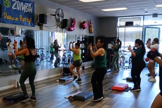 Zumba Dance Party fitness class with participants exercising on step platforms in a bright studio with mirrors and equipment