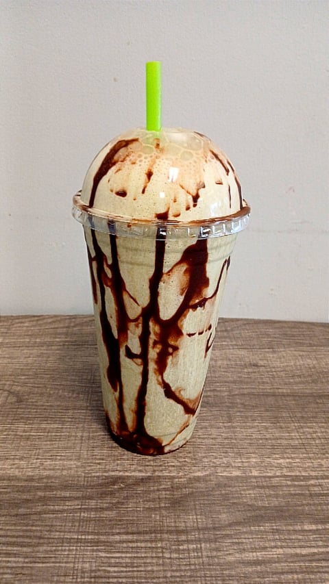 Iced coffee drink in plastic cup with chocolate drizzle and green straw on wooden surface