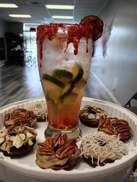 A decorative cocktail with red glitter rim and lime slices, surrounded by assorted chocolate pastries on a white plate