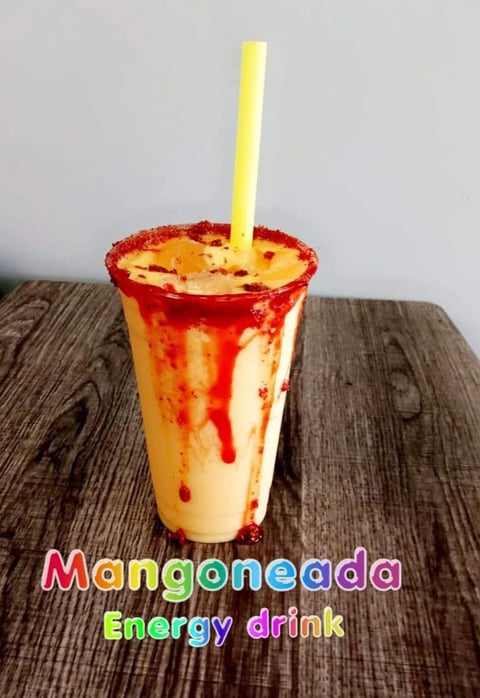 Manganegada energy drink in a clear cup with red sugar rim and yellow straw on wooden surface
