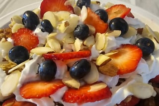 White plate with whipped cream topped with fresh strawberries, blueberries, and sliced almonds