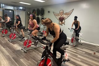 Group of women exercising on stationary bikes in a fitness studio with decorative wall art