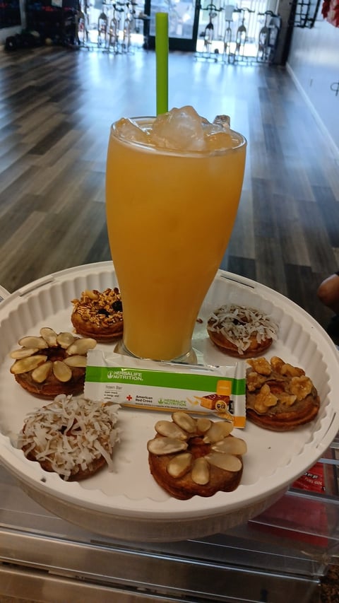 Orange juice with ice and green straw surrounded by small pastries with nuts and coconut on a white plate